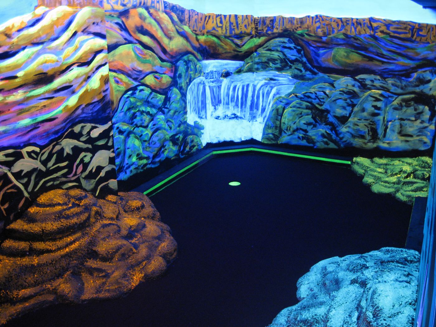 Glowing waterfall-themed hole on the blacklit indoor mini golf course at Glow Games in Twin Falls